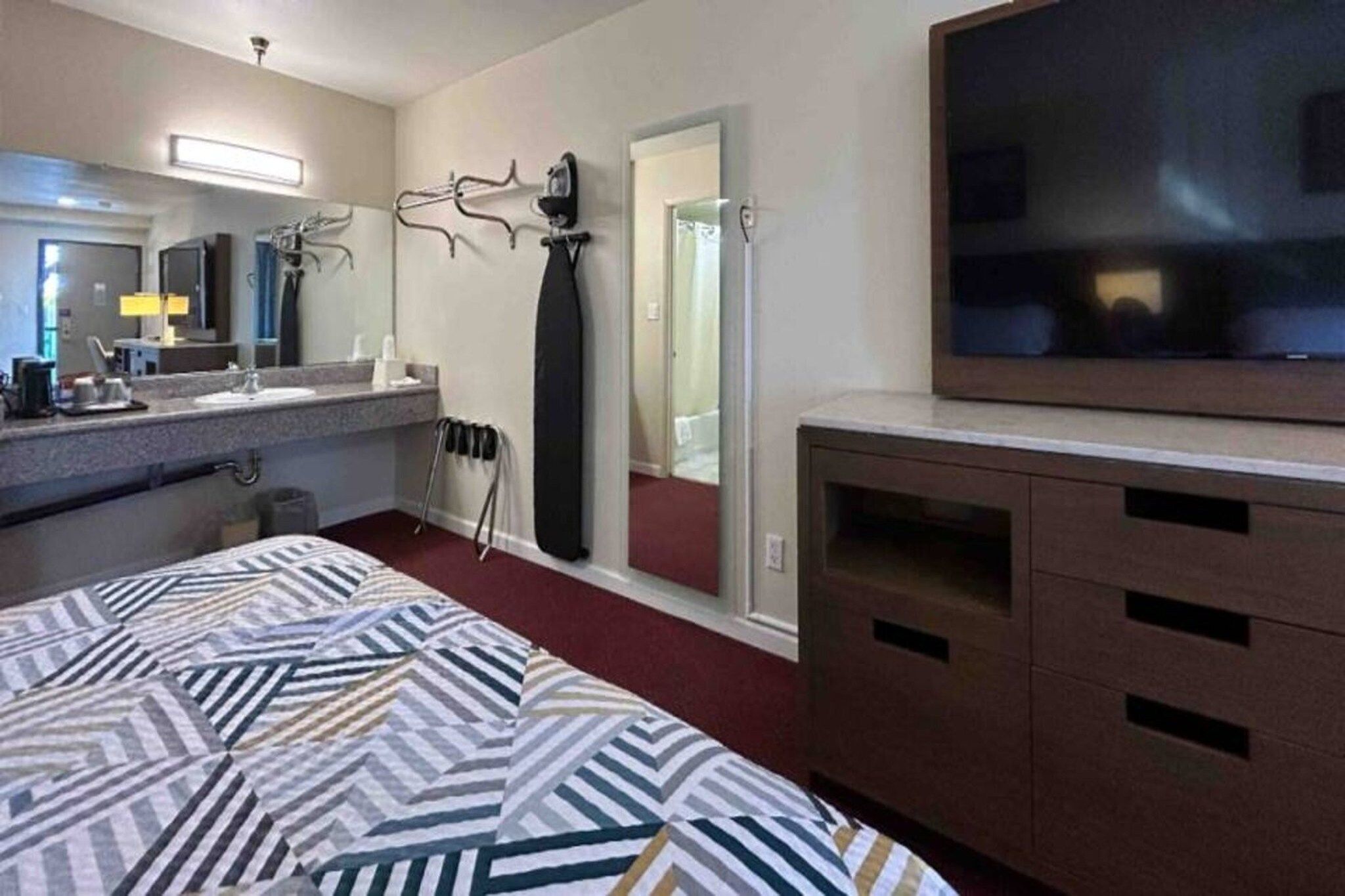 A hotel room with a bed, a TV, a bathroom with a shower, and a desk.