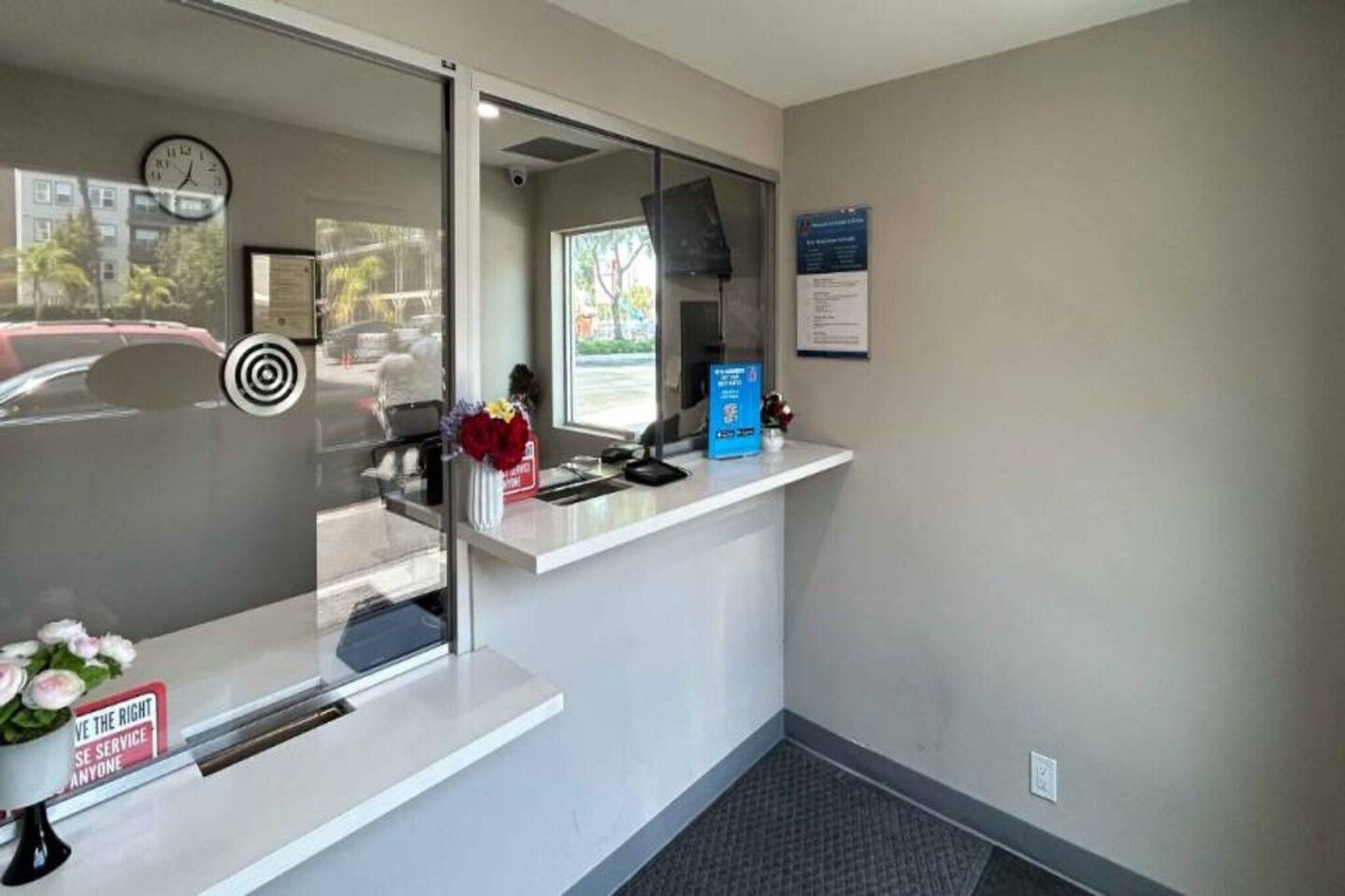 A reception area with a glass partition, a clock, a bulletin board, and a counter with a vase of flowers.