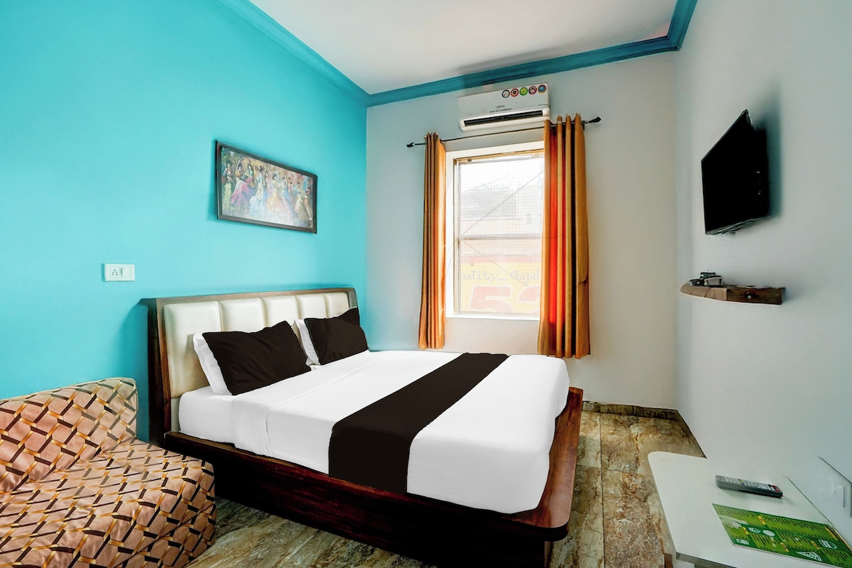 A hotel room with a bed, a TV, a window with curtains, a painting on the wall, and a small table.