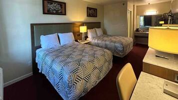 A hotel room with two beds, a desk, a chair, a lamp, and artwork on the walls.