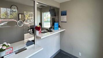A reception area with a glass partition, a clock, a bulletin board, and a counter with a vase of flowers.