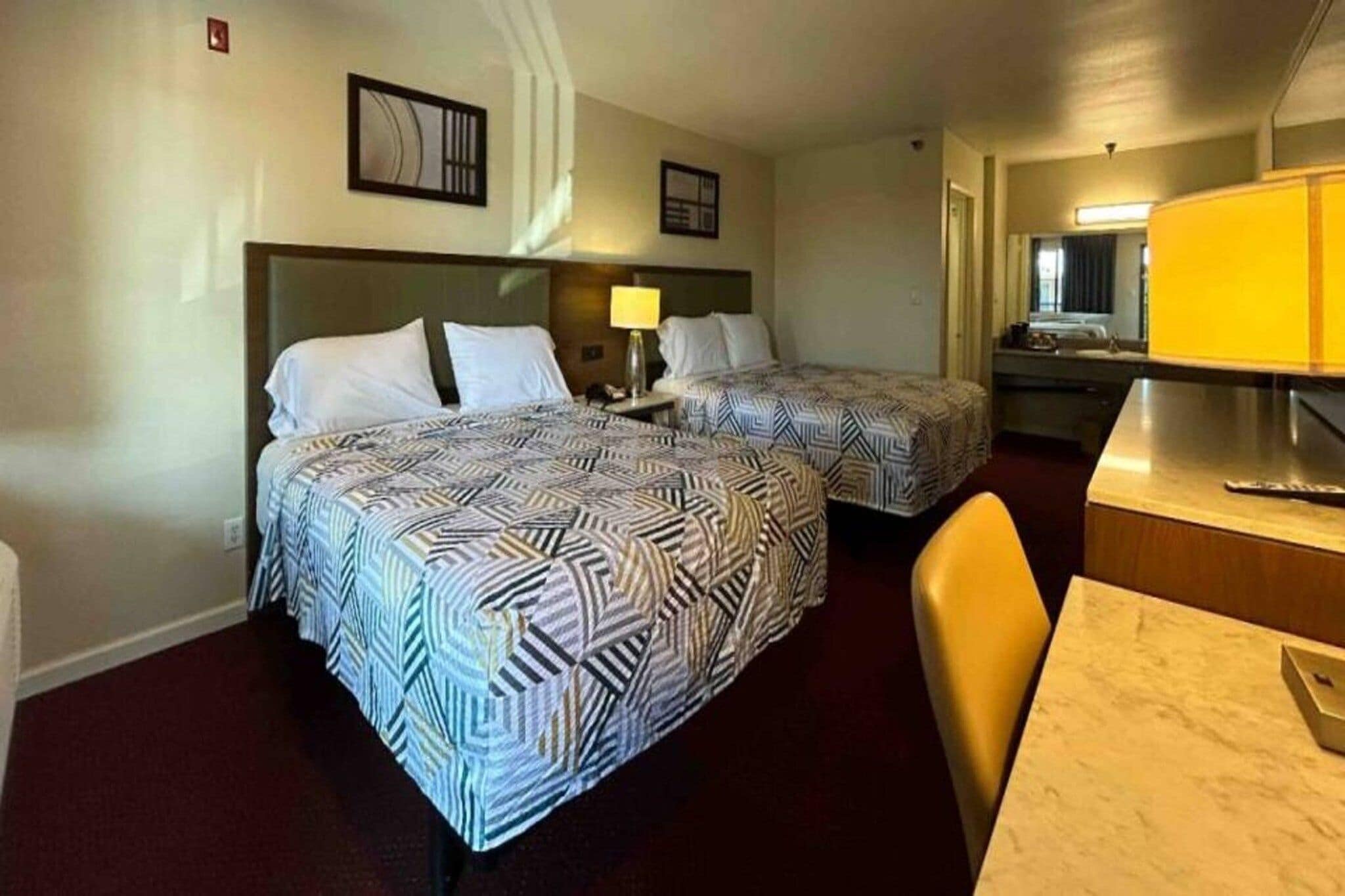 A hotel room with two beds, a desk, a chair, and a mirror.