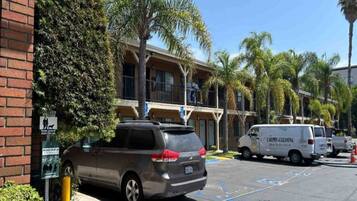 A parking lot with a grey minivan and a white van, surrounded by palm trees and a building with balconies.