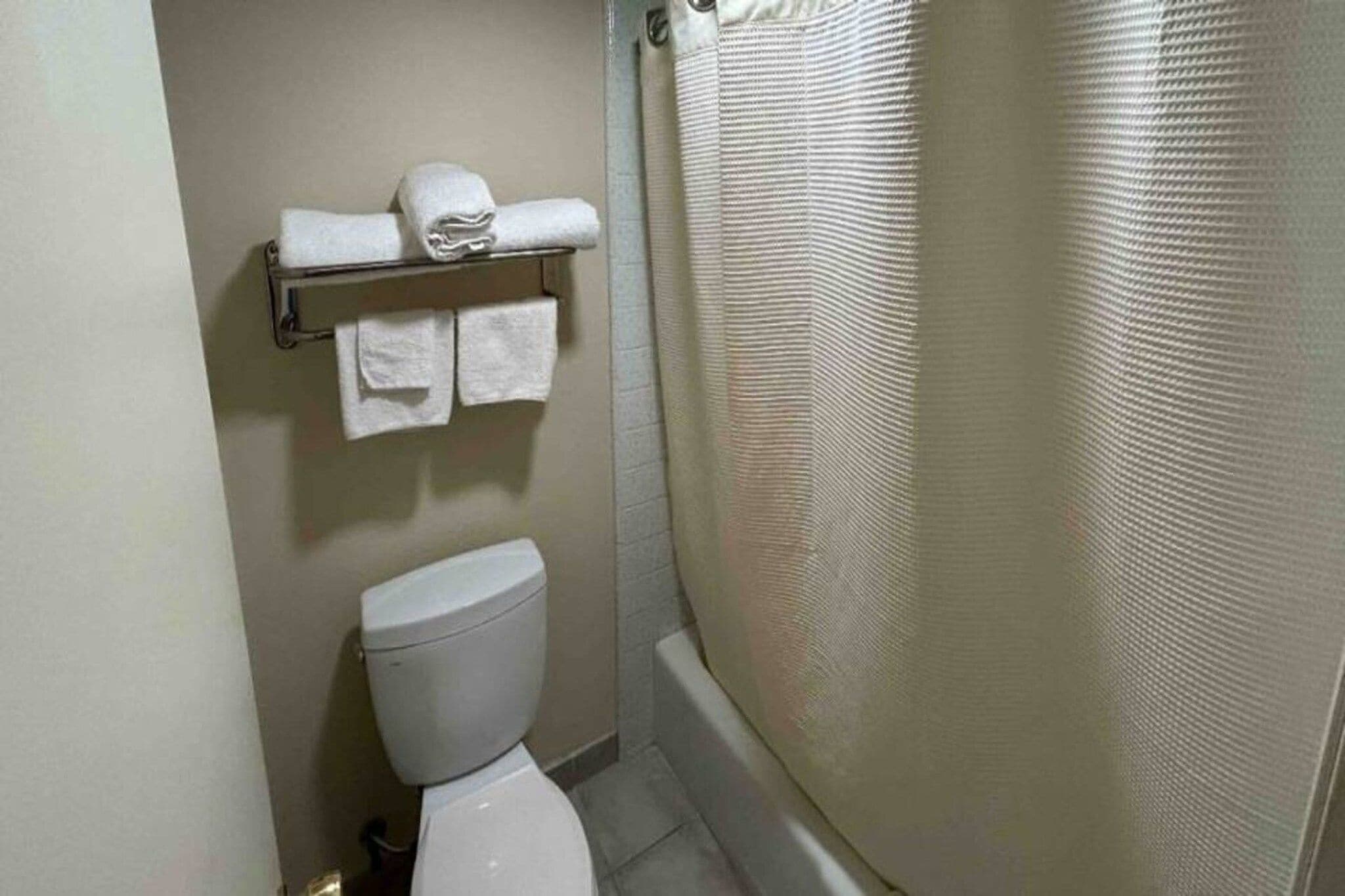Een compacte badkamer met toilet, een handdoekrek met opgevouwen handdoeken en een douchegordijn.