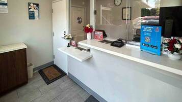 A reception area with a white counter, a clock on the wall, and a door leading to another room.