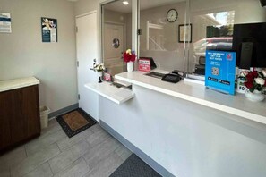 Een receptiegedeelte met een witte balie, een klok aan de muur en een deur naar een andere ruimte.