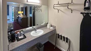 A hotel bathroom with a sink, mirror, towel rack, and a trash bin.