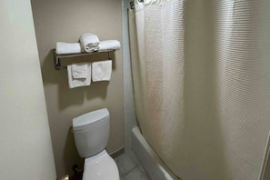 Een compacte badkamer met toilet, een handdoekrek met opgevouwen handdoeken en een douchegordijn.