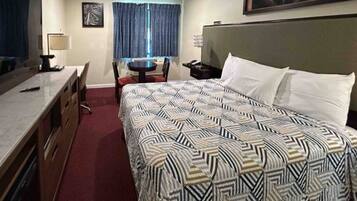 A hotel room with a bed, a desk, a chair, a television, and a window with curtains.