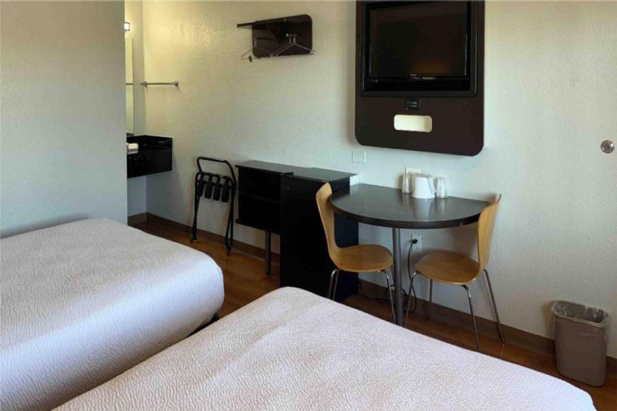 A hotel room with two beds, a desk, a chair, a TV, and a trash bin.