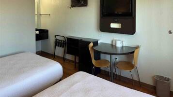 A hotel room with two beds, a desk, a chair, a TV, and a trash bin.