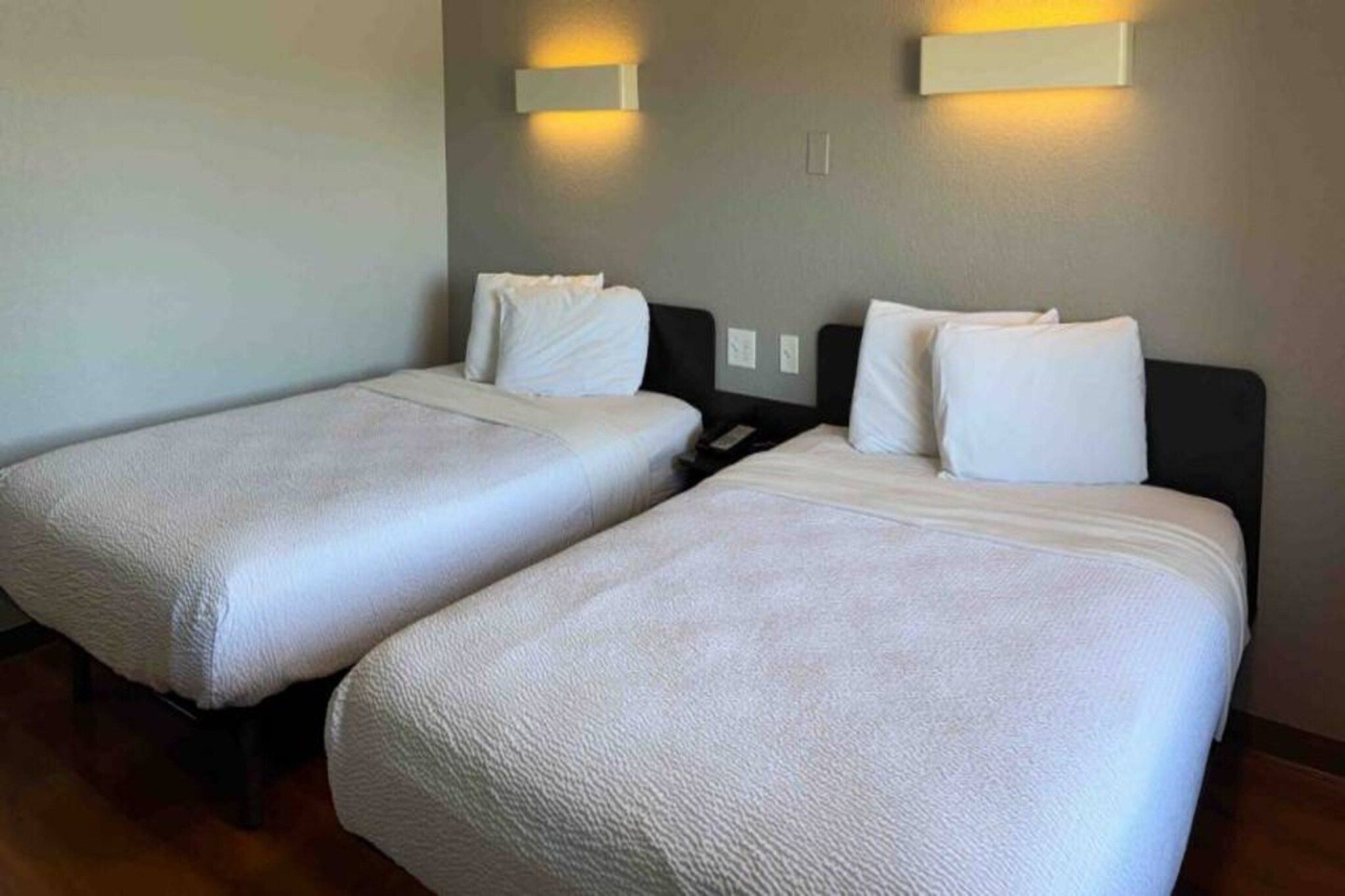 A hotel room with two single beds, each with a white duvet and pillows, and a nightstand between them.