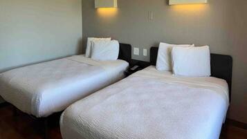 A hotel room with two single beds, each with a white duvet and pillows, and a nightstand between them.