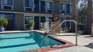 A swimming pool with a metal ladder, a wheelchair, and a red umbrella.