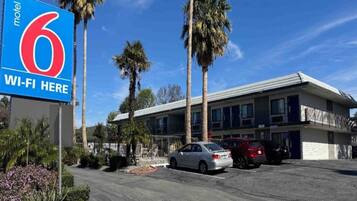 A motel with a sign indicating '6 Wi-Fi Here' and a parking lot with several cars.