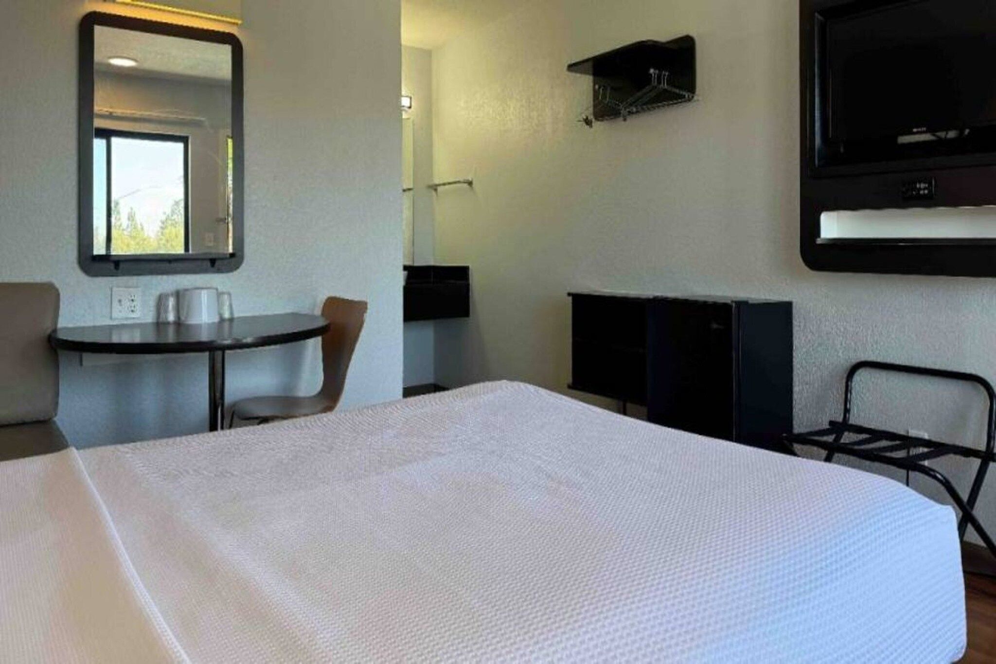 A hotel room with a bed, a desk, a chair, a TV, and a mirror.