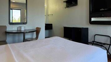 A hotel room with a bed, a desk, a chair, a TV, and a mirror.