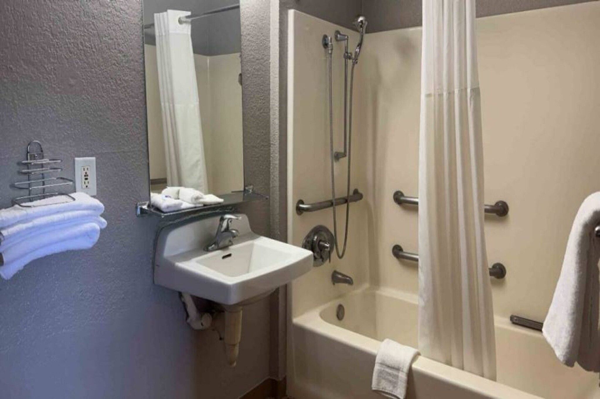 A bathroom with a sink, mirror, towel rack, and a shower area with a curtain.