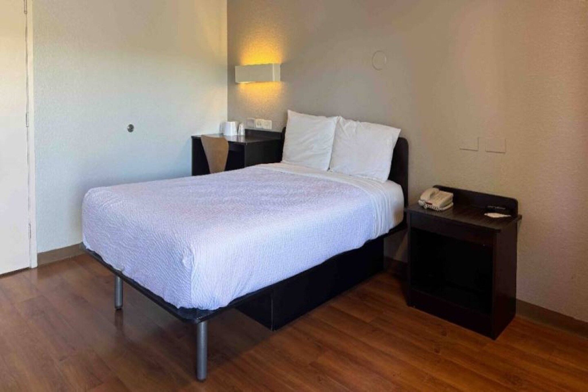 A single bed with a white bedspread in a room with wooden flooring.