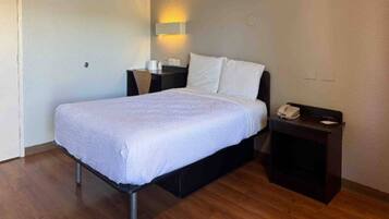 A single bed with a white bedspread in a room with wooden flooring.