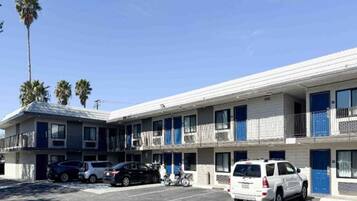 A multi-story motel with a parking lot, several cars parked, and palm trees in the background.