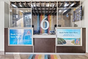 Una taquilla de recepció amb un gran cartell amb el número 6, dos cartells promocionals emmarcats i un disseny interior modern.