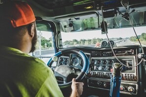 A person driving a vehicle with a steering wheel, dashboard, and various controls.