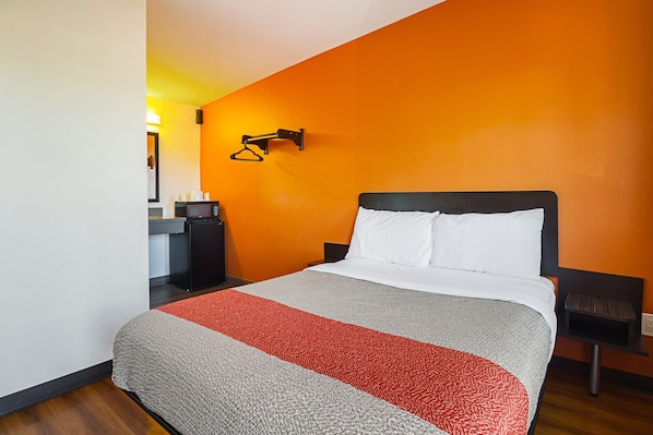A hotel room with a bed, a nightstand, a wall-mounted lamp, and a small table with a cup.