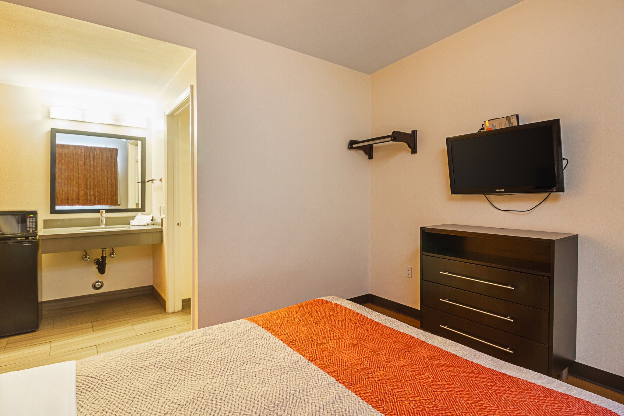 Een hotelkamer met een bed, een dressoir, een televisie en een badkamer zichtbaar door een geopende deur.