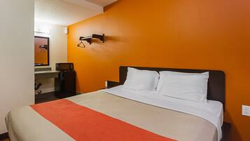 A hotel room with a bed, a microwave, a refrigerator, and a mirror.