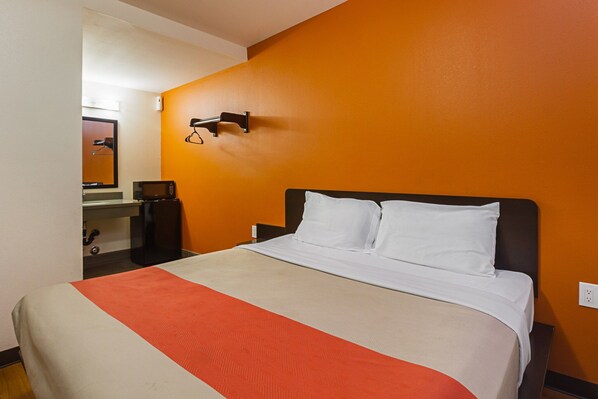 A hotel room with a bed, a microwave, a refrigerator, and a mirror.