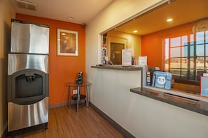 A hotel room with a minibar, a small table, a chair, a window with a view, and a reception area with a counter and a computer. - 1 Queen Bed | Non-Smoking, Micfridge (Hesperia)