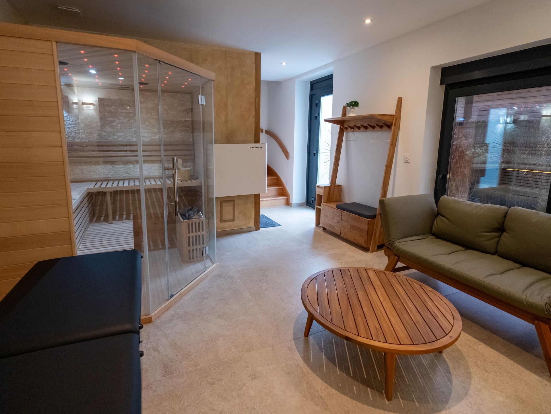 Een moderne woonkamer met een sauna met glazen wanden, een houten bankje, een ronde houten tafel en een bank.