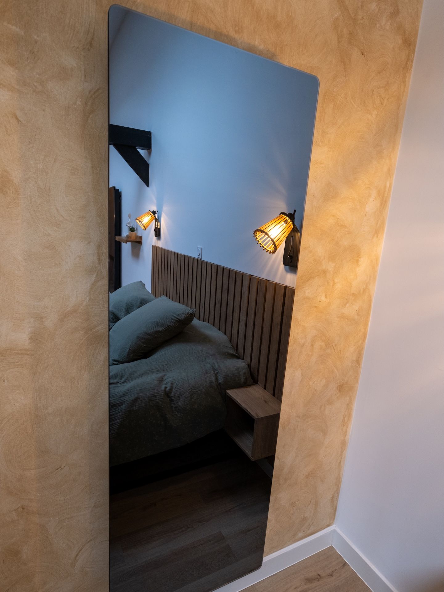 Een slaapkamer met een schuine kap, een houten hoofdbord en twee wandlampen.