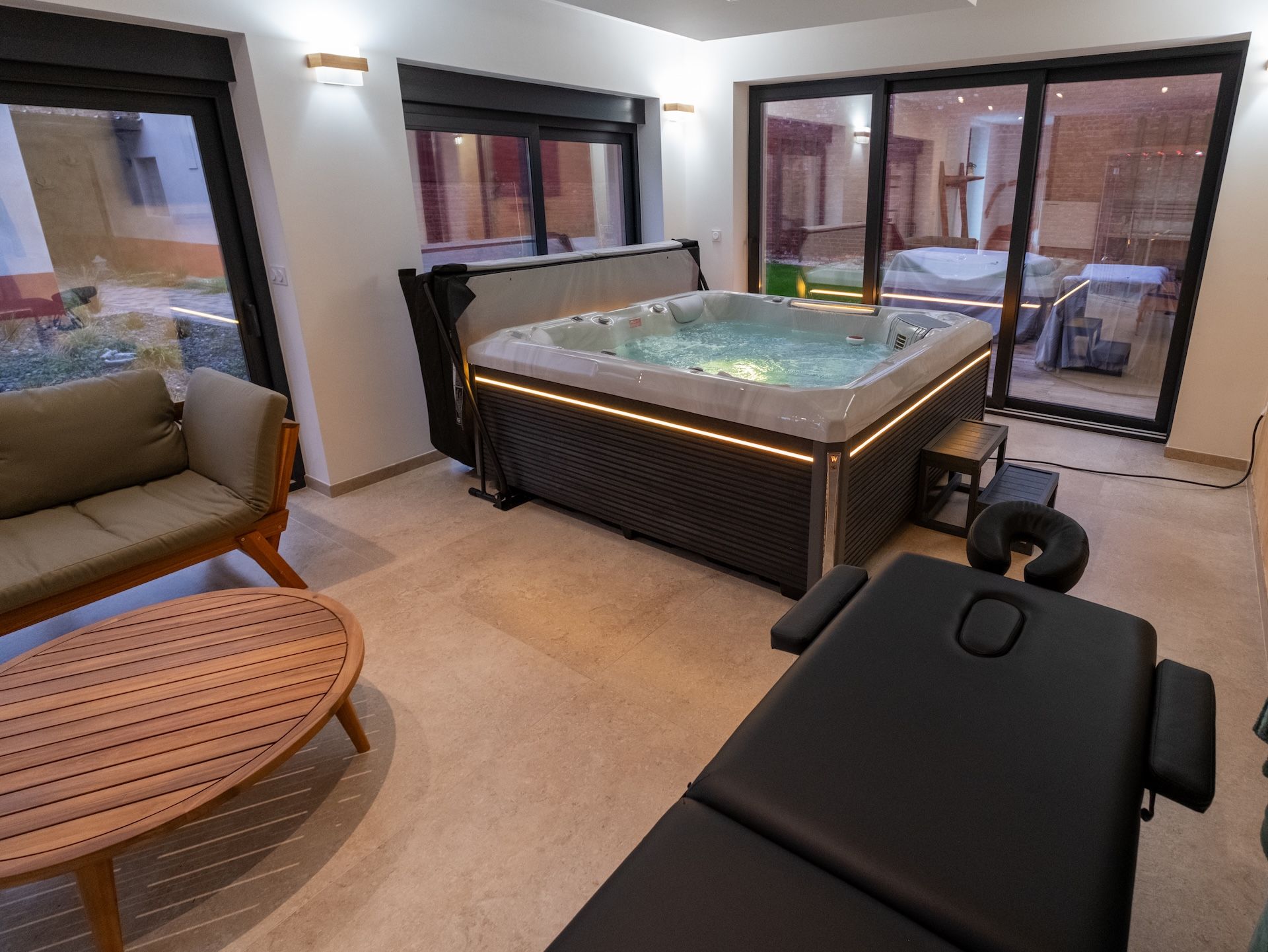 A modern spa room with a hot tub, a massage table, and a wooden table.