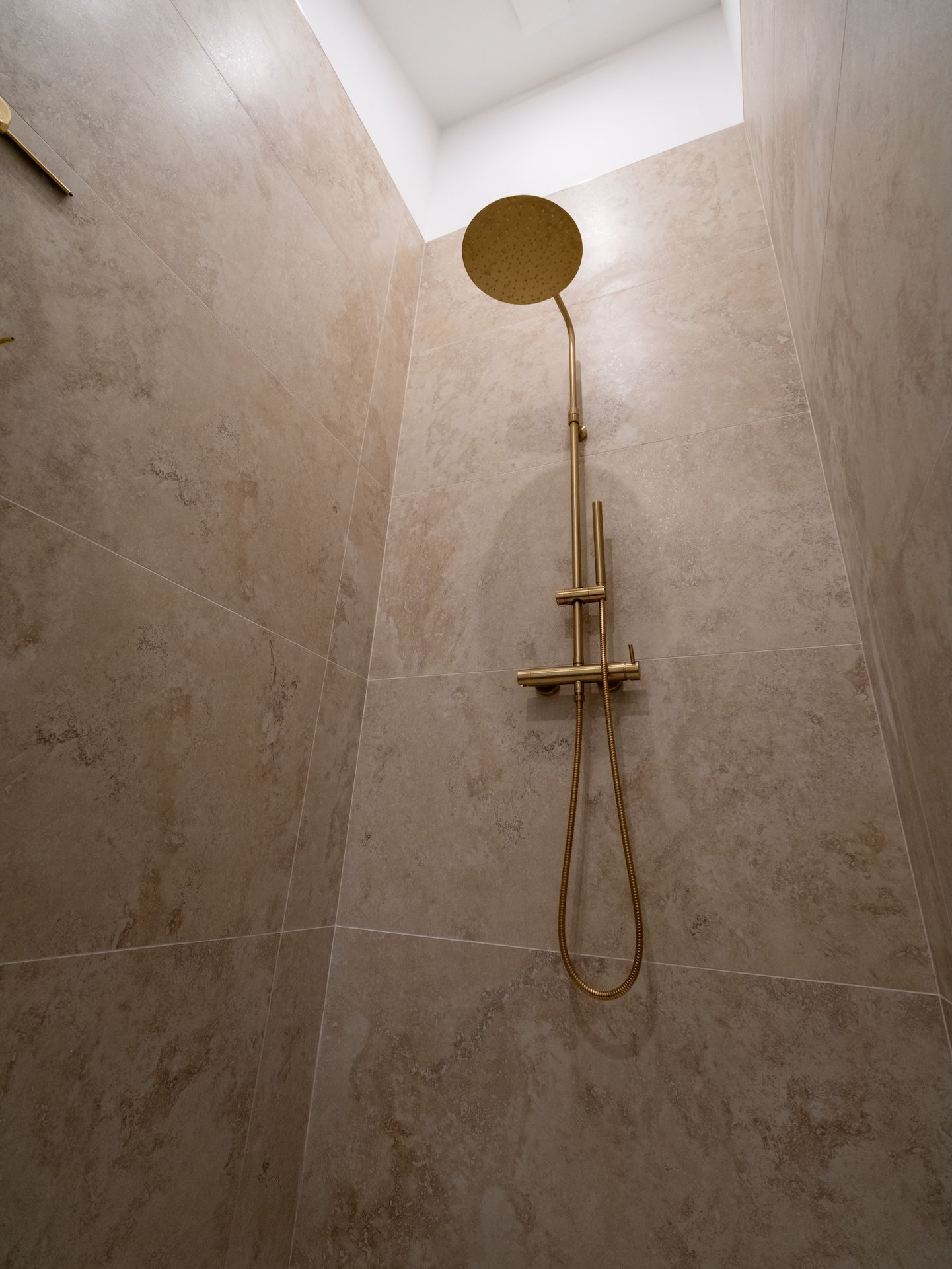 Een douche met een handdouche en een bedieningspaneel aan de muur.