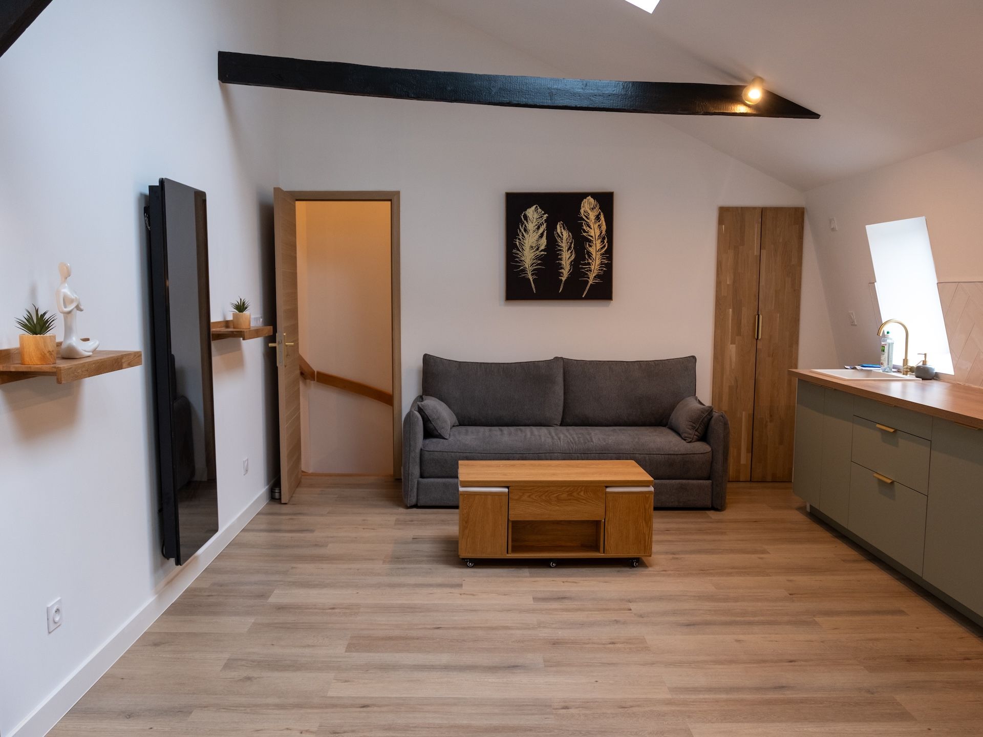 A modern living room with a grey sofa, wooden coffee table, and a painting of feathers on the wall.