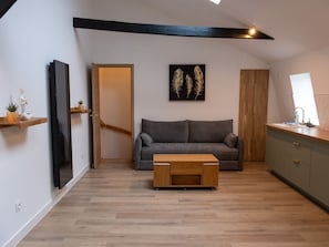 A modern living room with a grey sofa, wooden coffee table, and a painting of feathers on the wall.