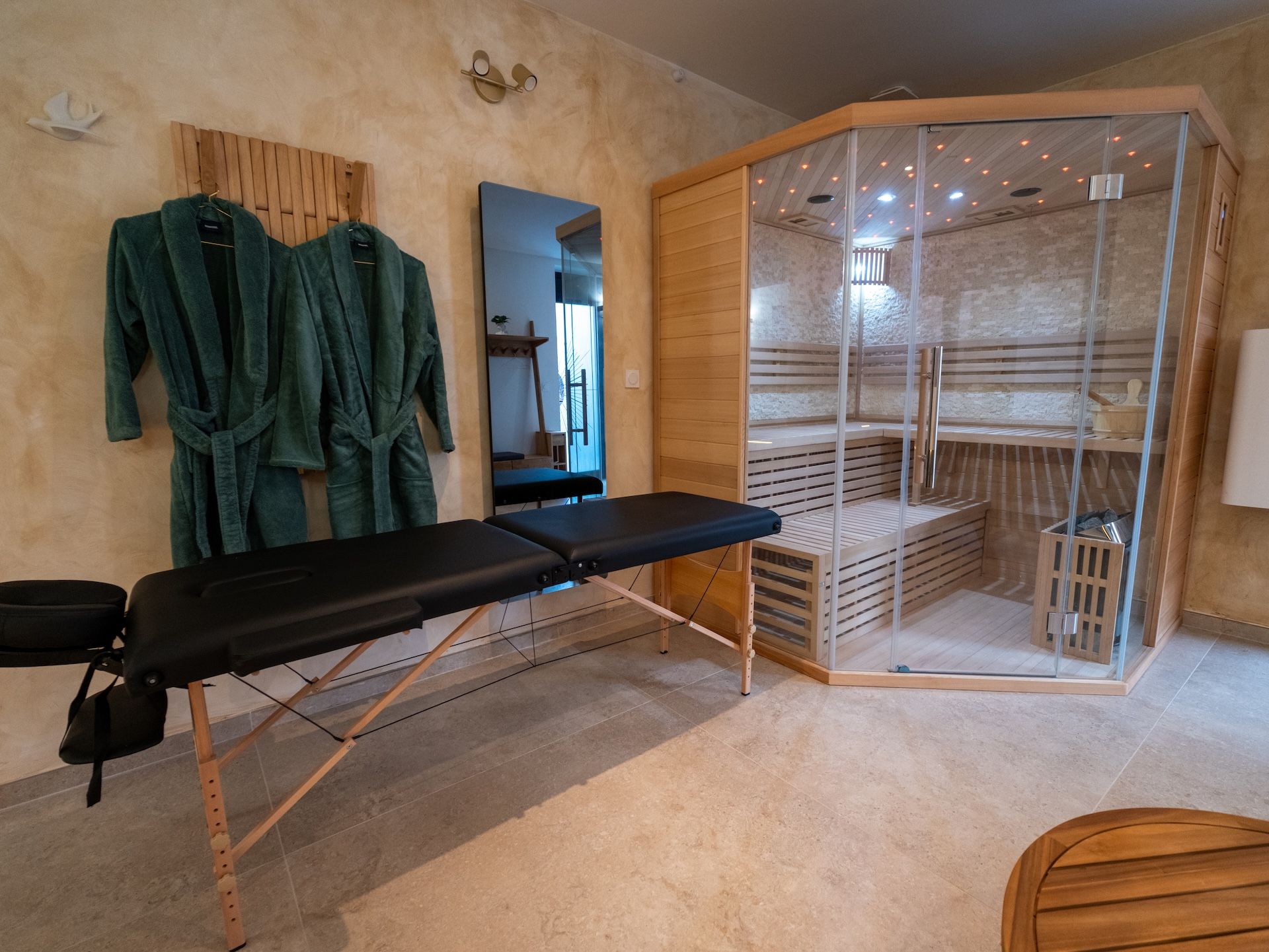 A room with a massage table, wooden benches, a glass shower enclosure, and a mirror.