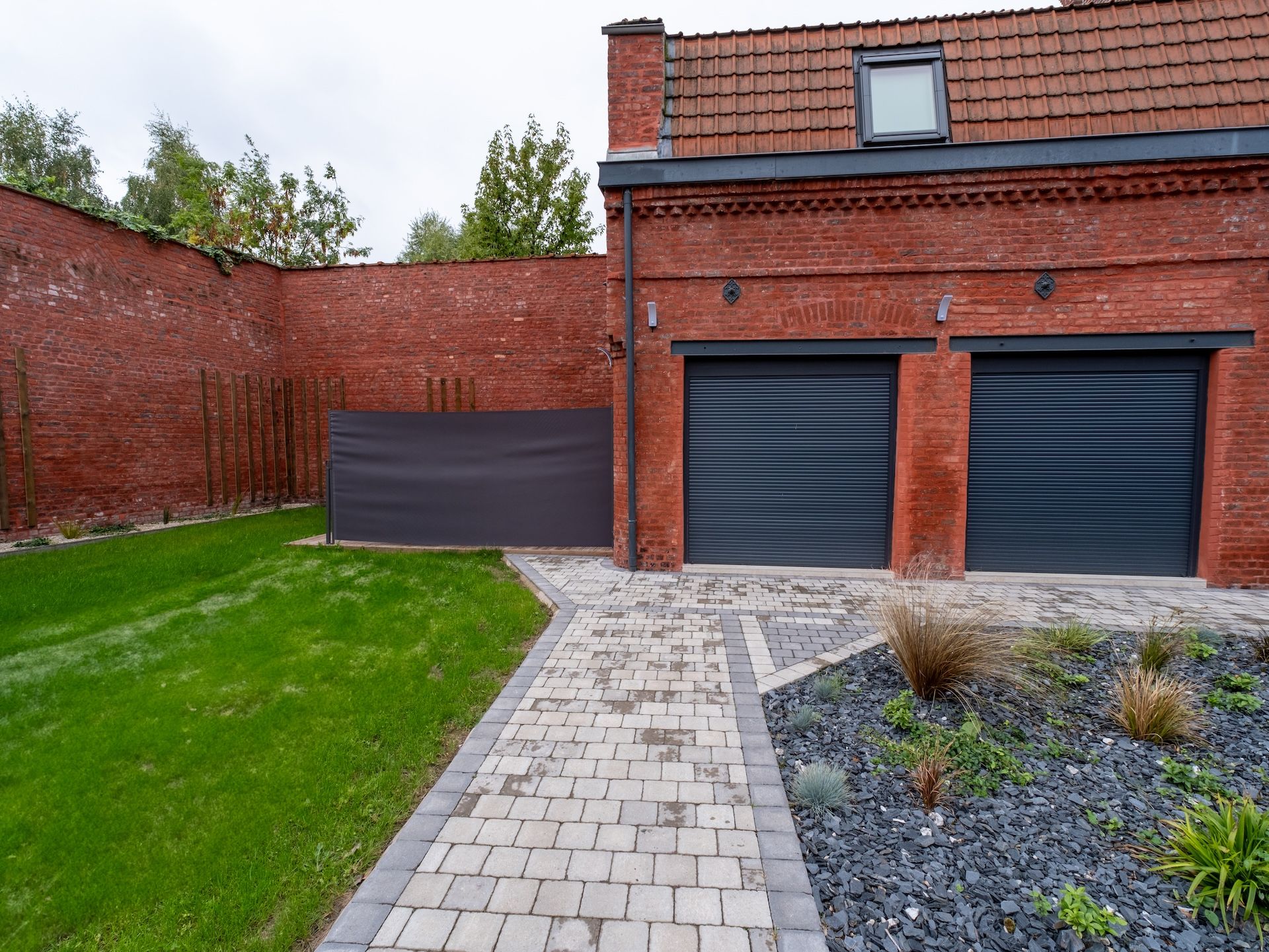 A brick building with two garage doors, a paved driveway, and a grassy area.