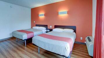 A hotel room with two beds, wooden flooring, a red curtain, and a wall-mounted heater.