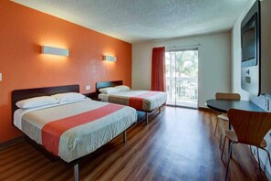 A hotel room with two beds, a dining table, and a TV. - 2 QUEEN BEDS | ADA/ROLL-IN SHOWER (SANTA ANA)