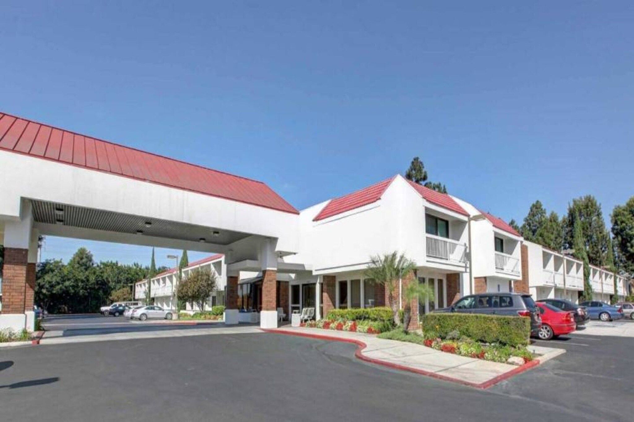 A hotel with a red roof, a covered parking area, and a landscaped entrance.