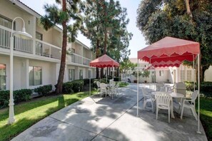 A courtyard with outdoor seating, a red canopy, and a building with balconies. - 1 KING BED | PREMIUM, MINI FRIDGE (SANTA ANA)