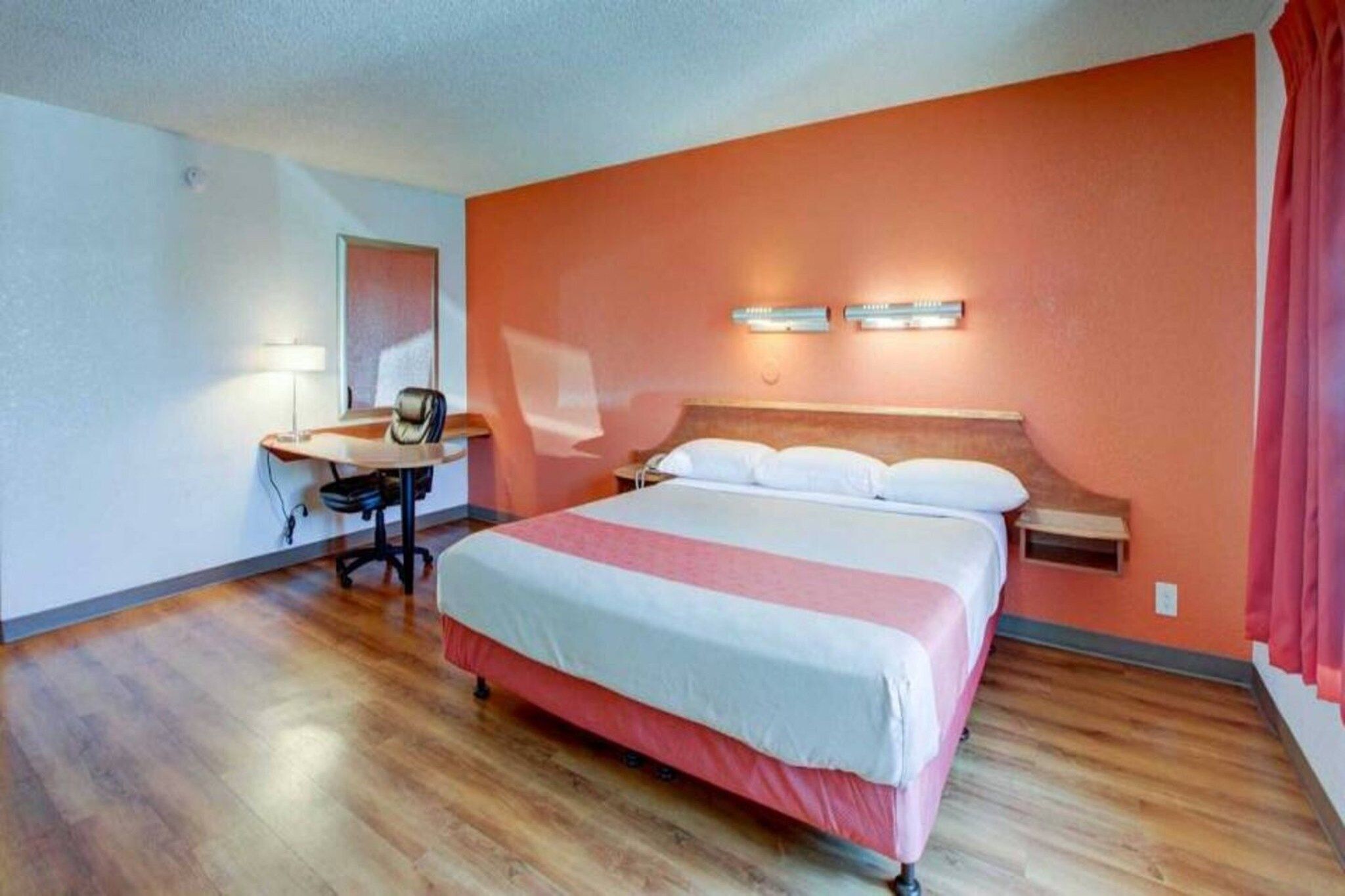 A hotel room with a bed, desk, chair, and a desk lamp.