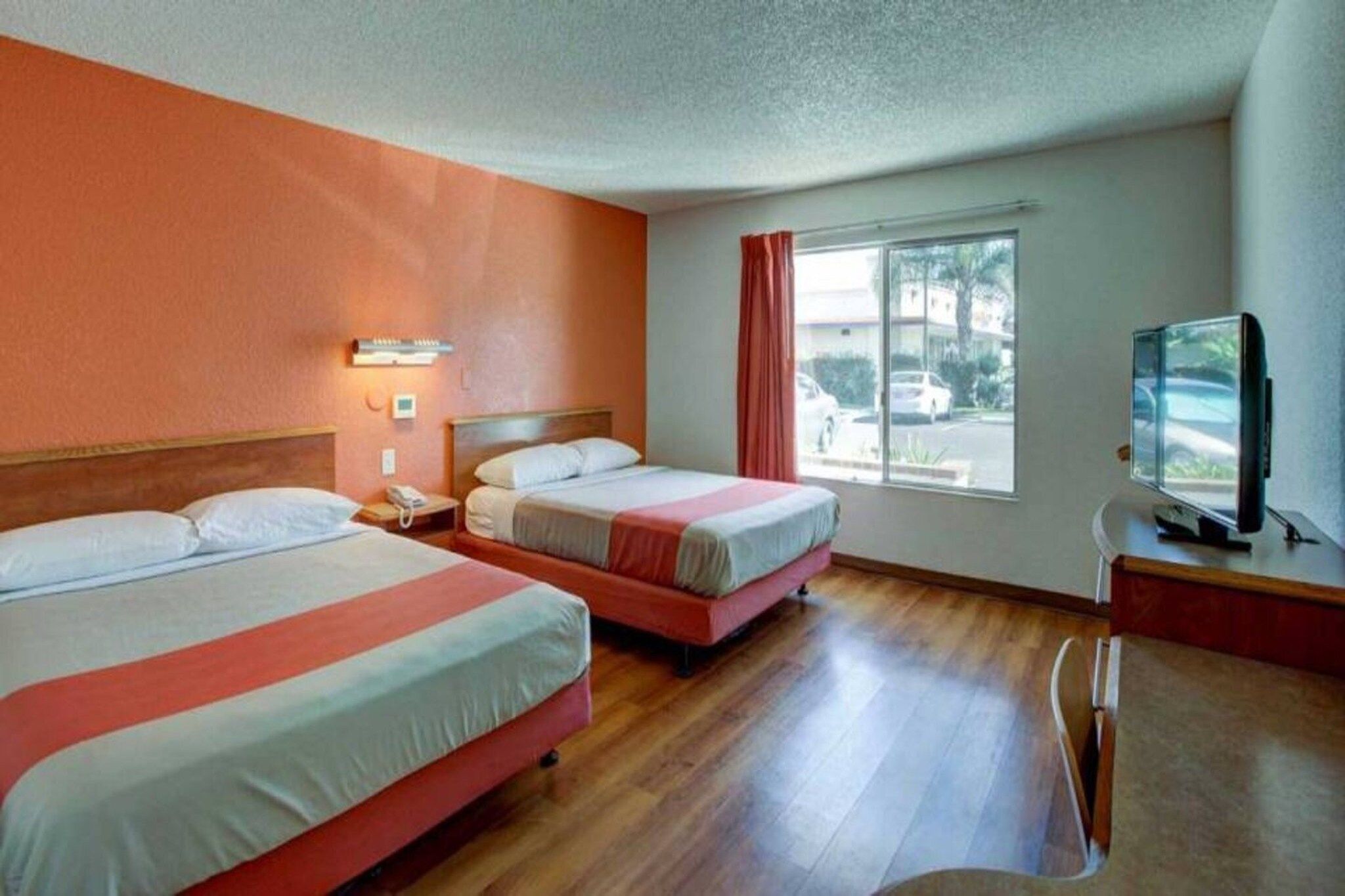 Habitación de hotel con dos camas, un escritorio con televisor y una ventana que da a la calle.
