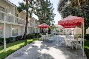 Un patio con mesas al aire libre, un toldo rojo y un edificio con balcones.