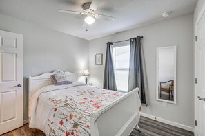 A bedroom with a bed, a ceiling fan, a window with curtains, a bedside lamp, and a door. - 7 Mi to Beach! Group & Pet-Friendly Palm Coast Gem (Palm Coast)