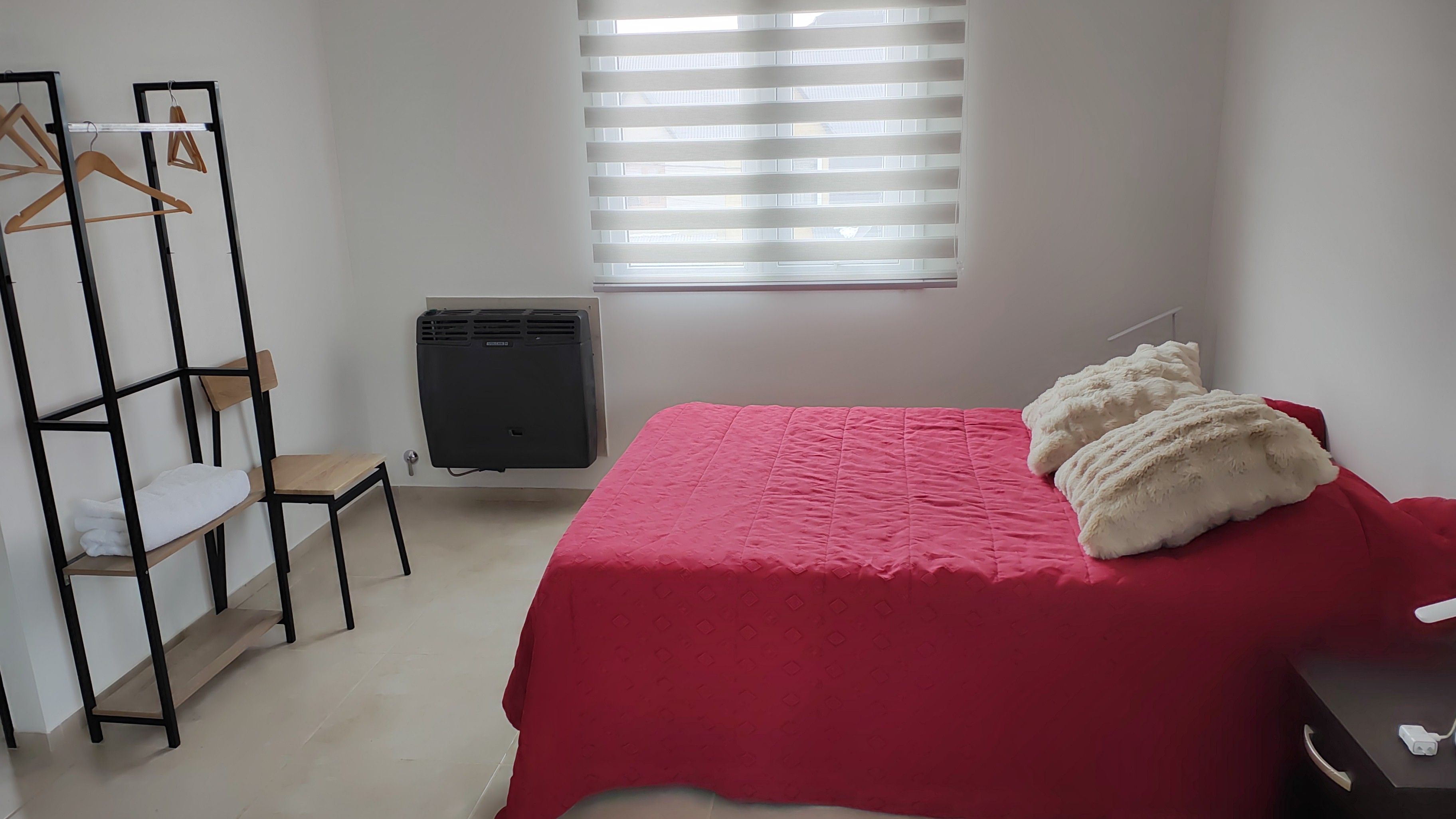 Ein Schlafzimmer mit einem Bett, einem Heizkörper, einem Holzschrank und einem Fenster mit Jalousien.