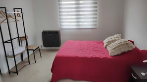 Quarto com cama, radiador, guarda-roupa de madeira e janela com persianas.